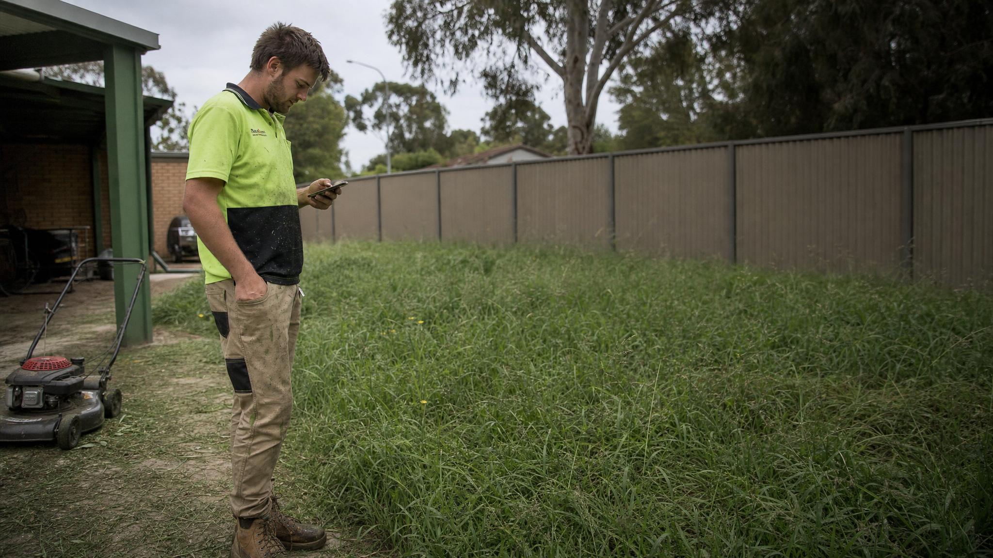A small operator standing in a yard, phone in hand, sizing up a job to work out a price